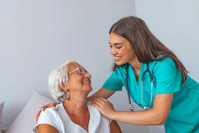 Resident and nurse review a medication list and appointment calendar at a table in an assisted living room.
